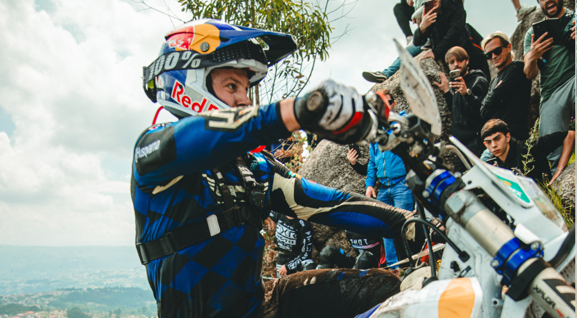 Hard Enduro rider muscling his bike up a rocky climb with fans watching